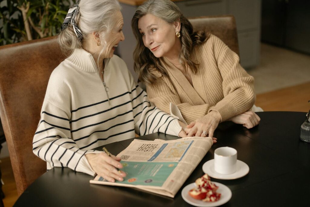 Two elderly women enjoying a cozy winter morning, sharing a heartfelt conversation over coffee and a newspaper for Galantine's day